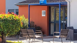 A hotel entrance with a blue awning, a signboard, and outdoor seating. - ibis budget Lyon Villefranche sur Saône (Limas)