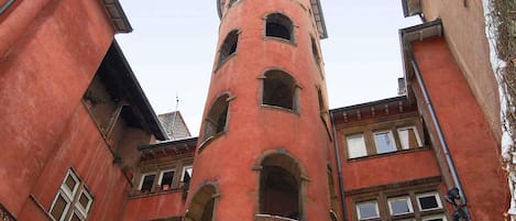 Un edificio de varios pisos con una torre central, ventanas arqueadas y fachada roja.