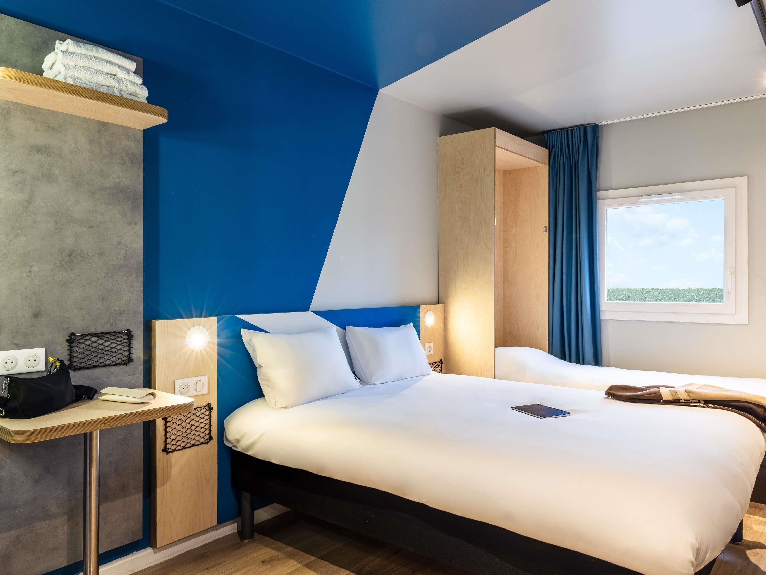 A hotel room with a bed, bedside table, lamp, and a window with curtains.