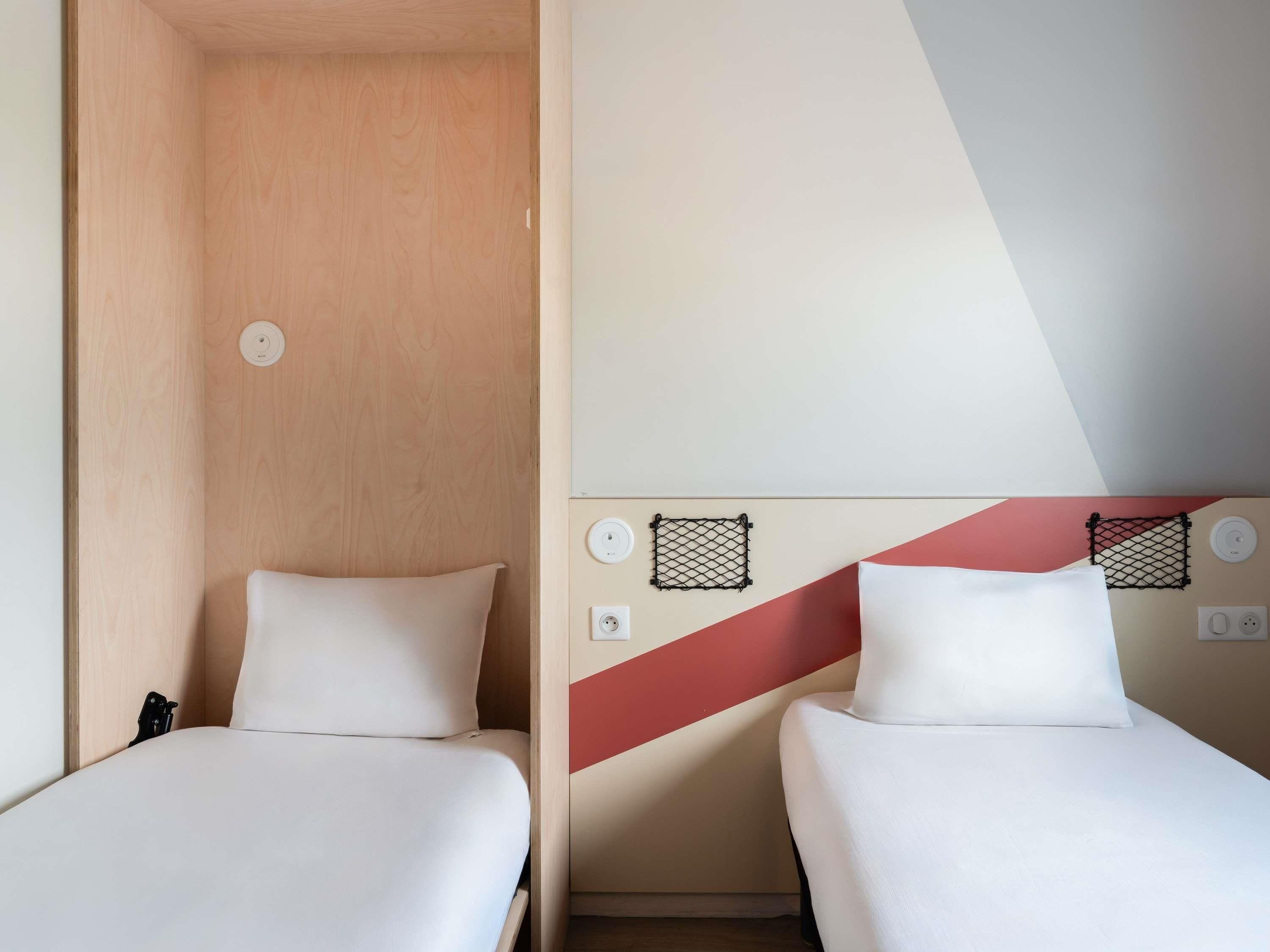 Habitación de hotel con dos camas individuales, un armario de madera y una pared con diseño geométrico.