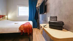 Une chambre d’hôtel avec un lit, un bureau, une télévision et une fenêtre avec des rideaux.