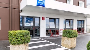 A modern building with a sign for 'ibis budget hotels' and a crosswalk leading to the entrance. - ibis budget Villemomble (Villemomble)