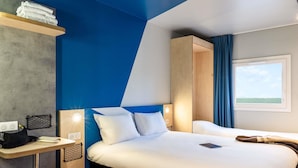 A modern hotel room with a large bed, a desk with a chair, a small table, and a window with a view. - ibis budget Villemomble (Villemomble)