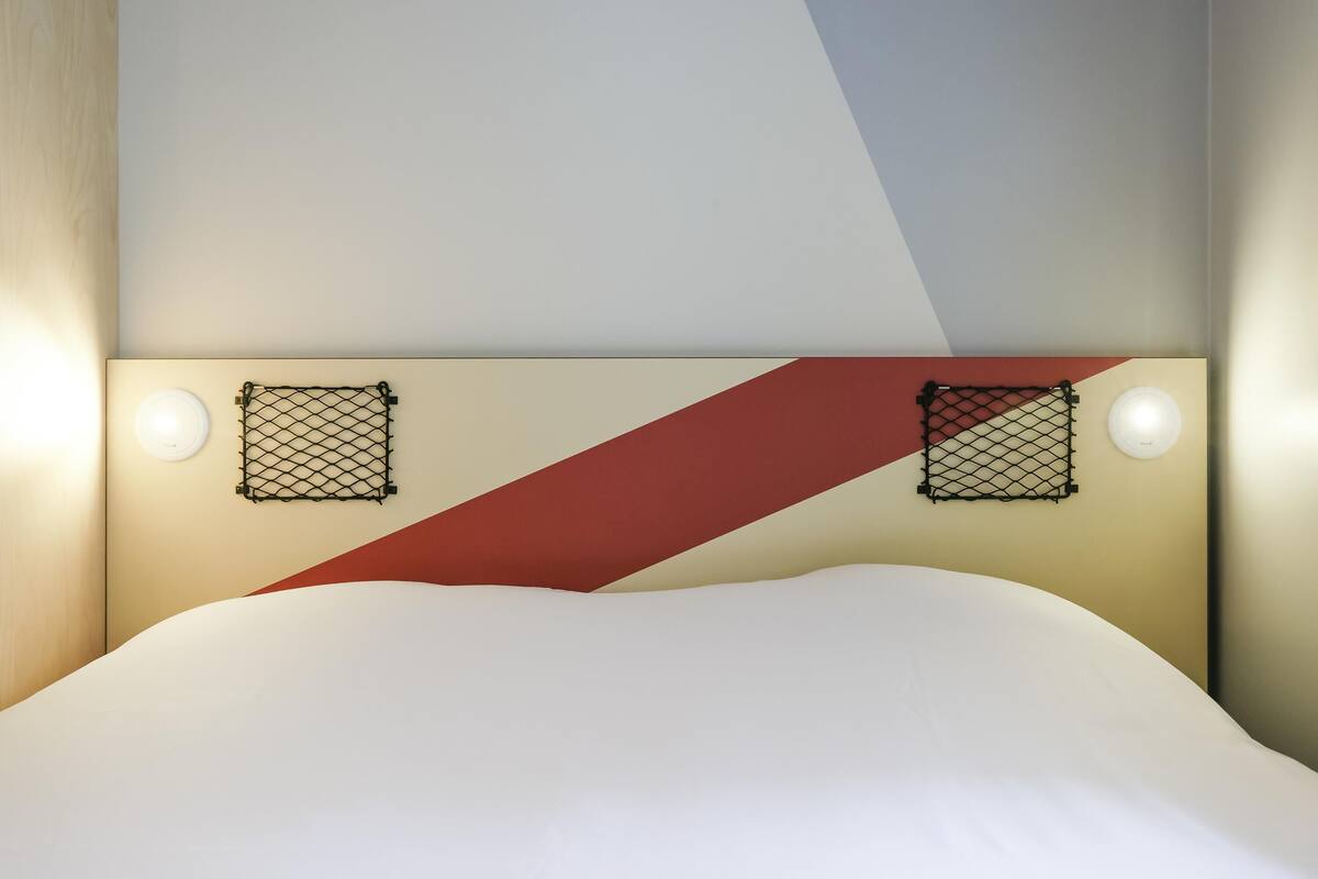 A bed with a white headboard, two wall-mounted light fixtures, and a geometric wall design.