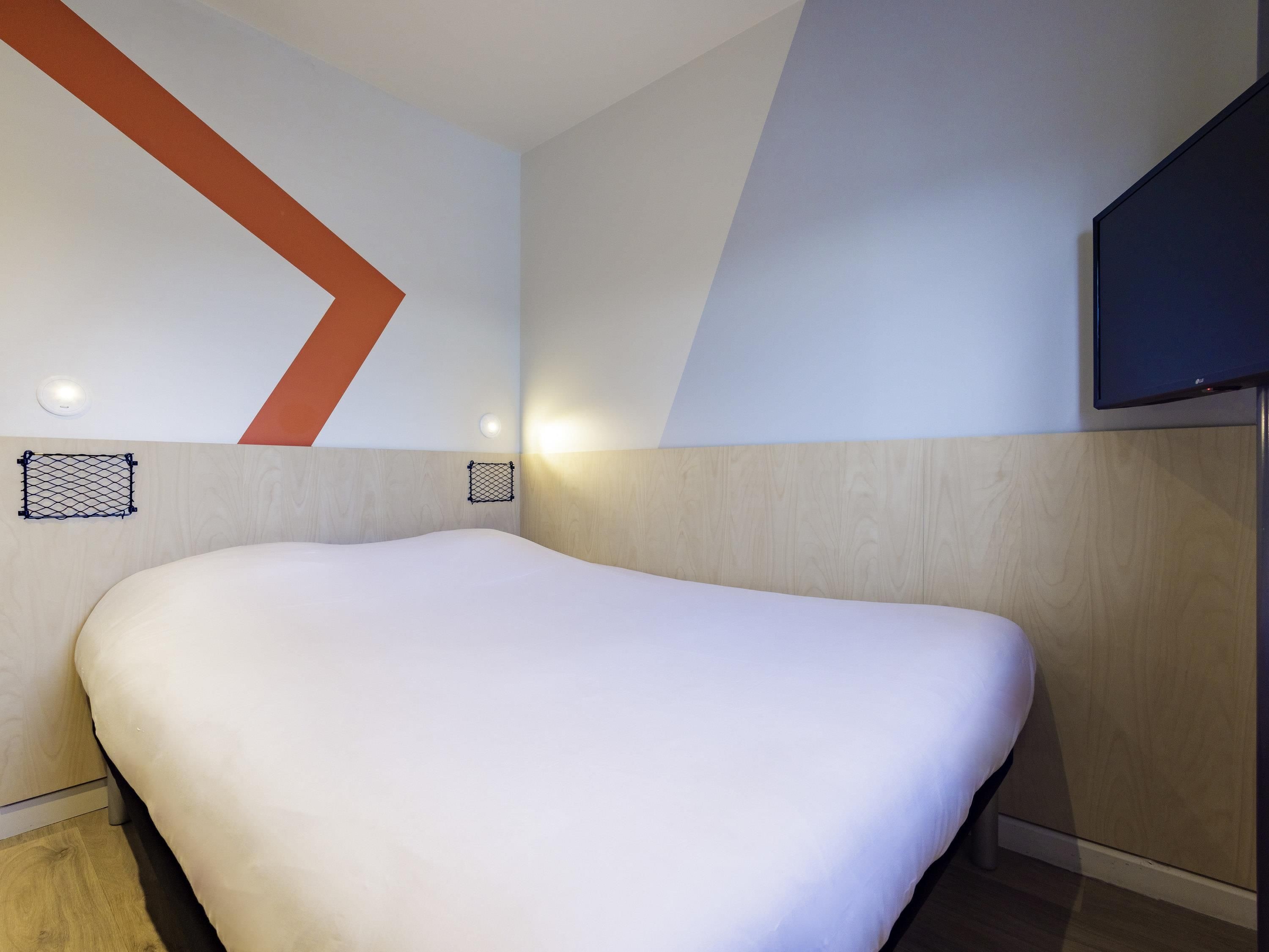 Una habitación de hotel moderna con una cama grande, un televisor de pantalla plana en la pared y un diseño geométrico único en la pared.