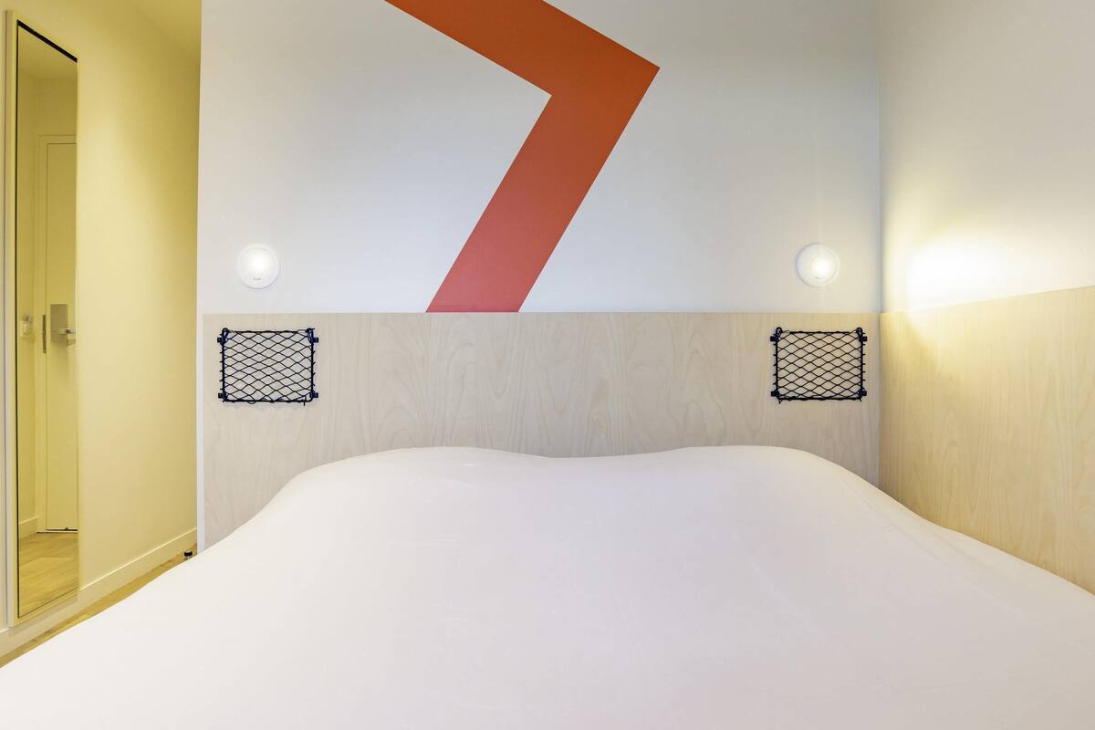 A hotel room with a bed, a large geometric wall decoration, and two wall-mounted light fixtures.