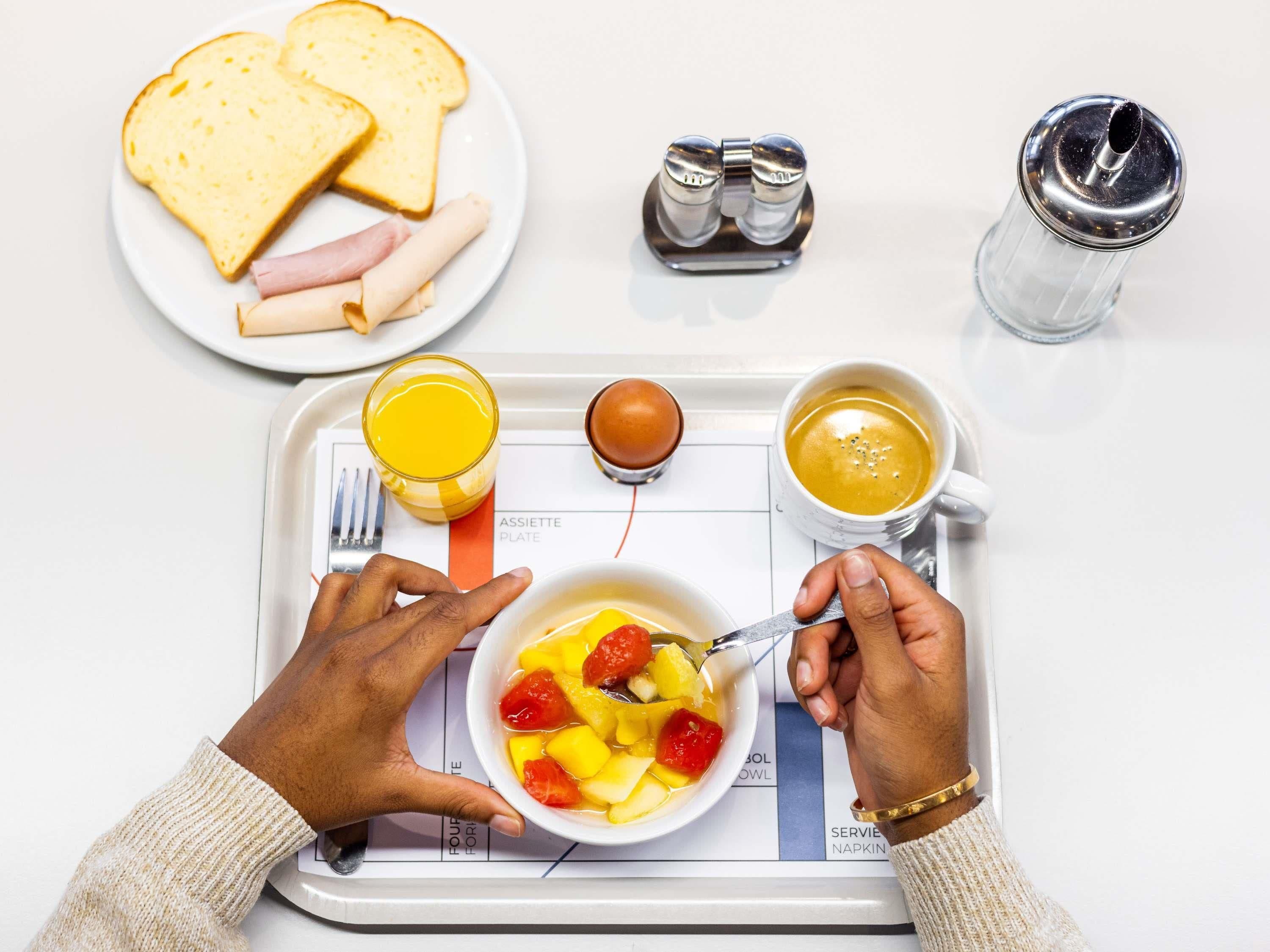 A tray with breakfast items including toast, ham, fruit, a glass of orange juice, a cup of coffee, and a salt shaker.