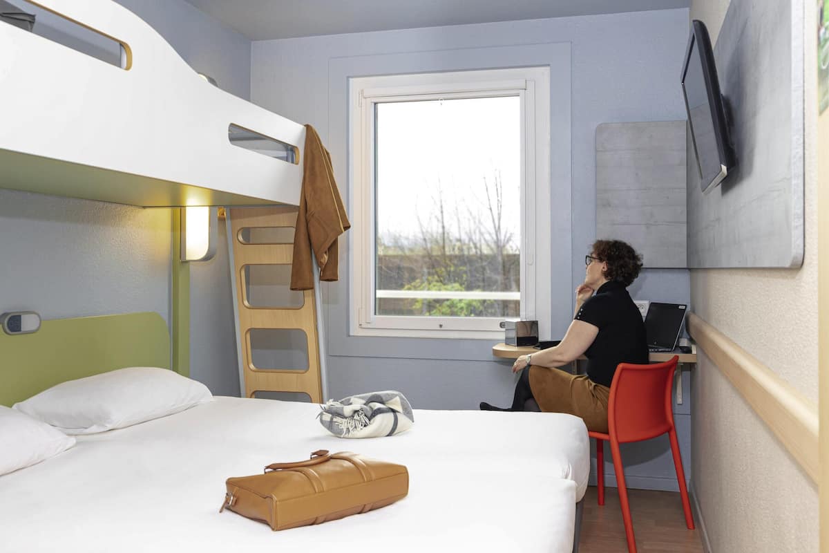 Um quarto com beliches, uma escrivaninha, uma cadeira, um laptop e uma janela.