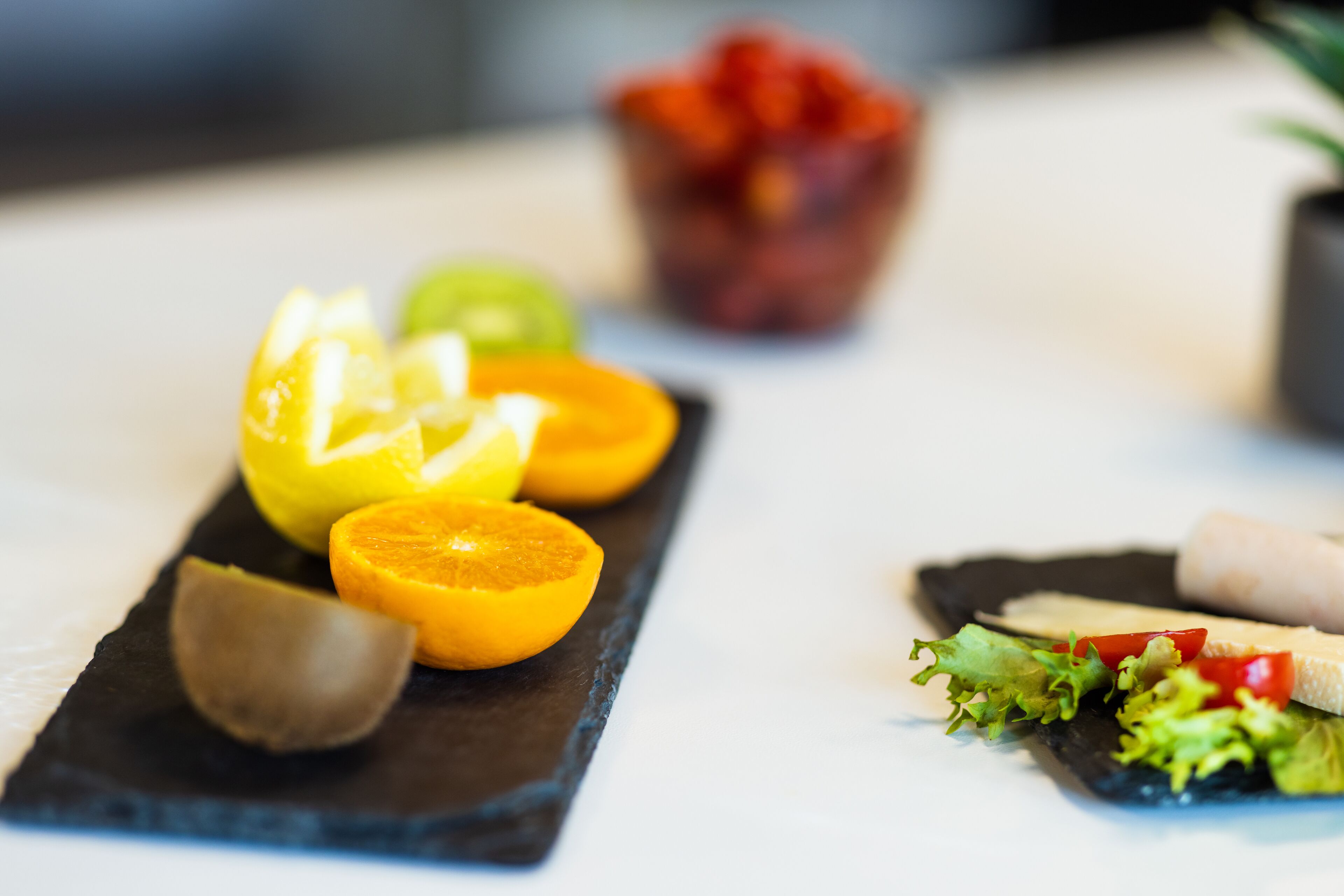 Una tabla de pizarra negra con frutas cítricas en rodajas y un cuenco pequeño de bayas rojas.