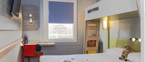 Habitación de hotel pequeña con literas, un escritorio con silla, una ventana con vistas y un oso de peluche en la cama.