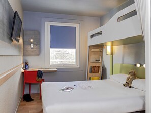 Ein kompaktes Hotelzimmer mit einem Etagenbett, einem Schreibtisch mit Stuhl, einem Fenster mit Blick und einem Teddybären auf dem Bett.
