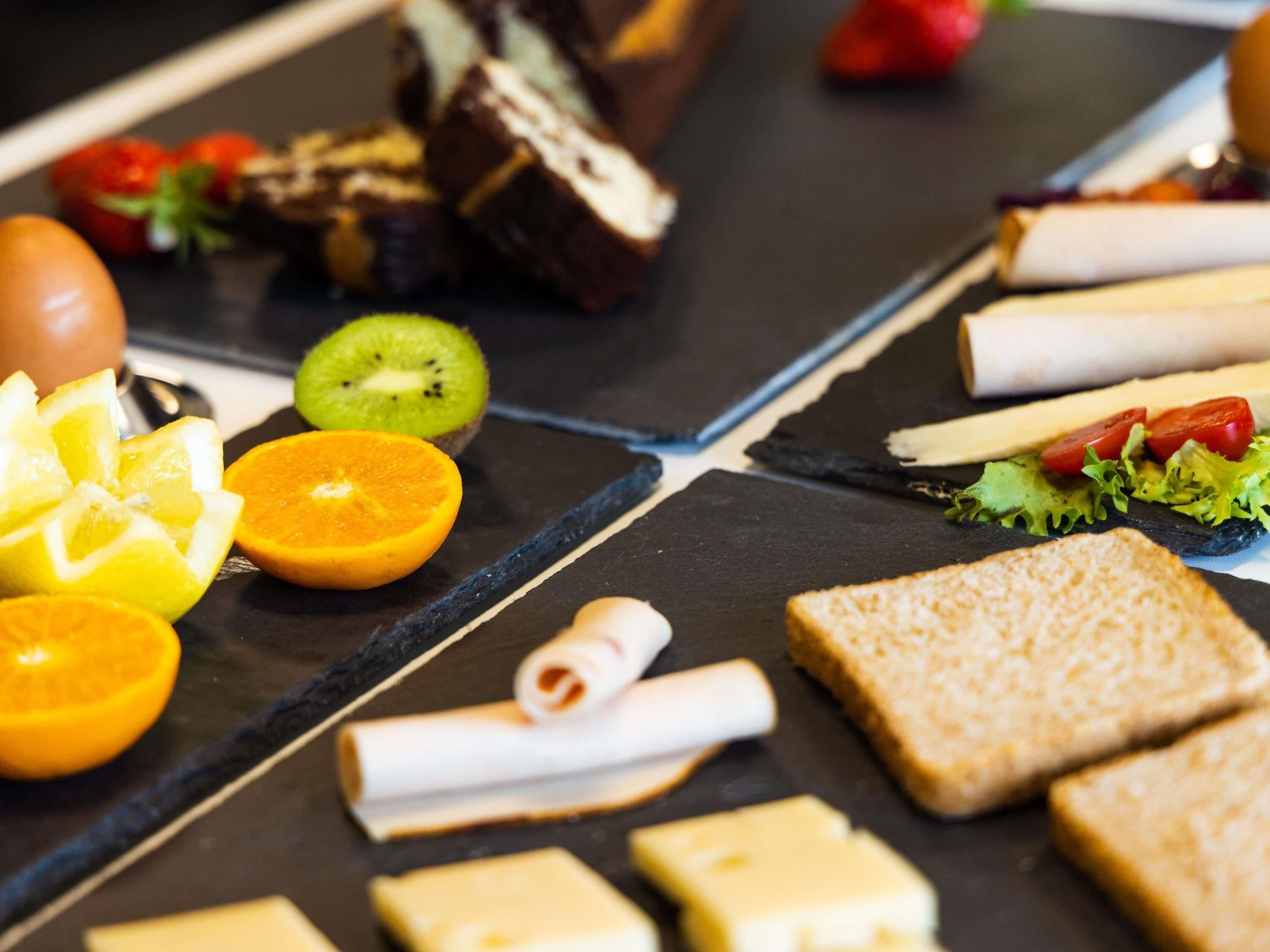 A variety of food items including sliced oranges, kiwi, cheese, and bread on a black slate surface.