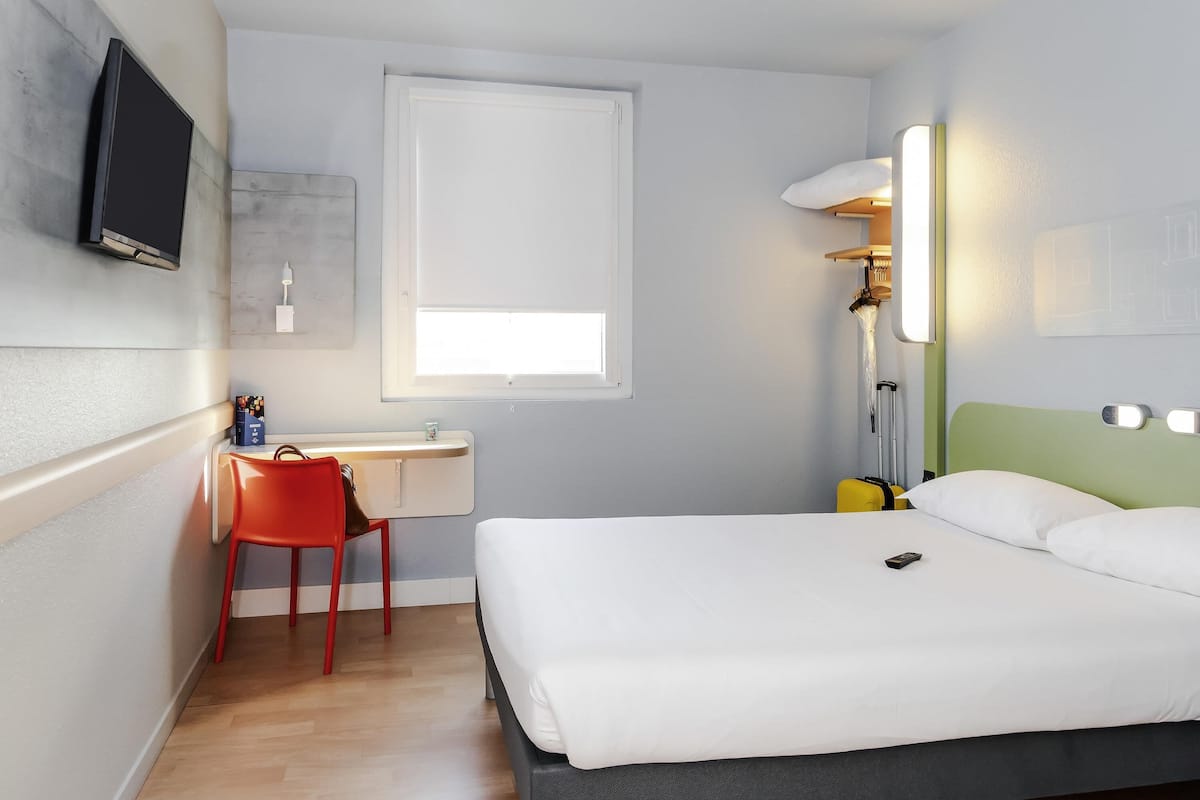 Een hotelkamer met een bed, een bureau, een stoel, een televisie en een raam.