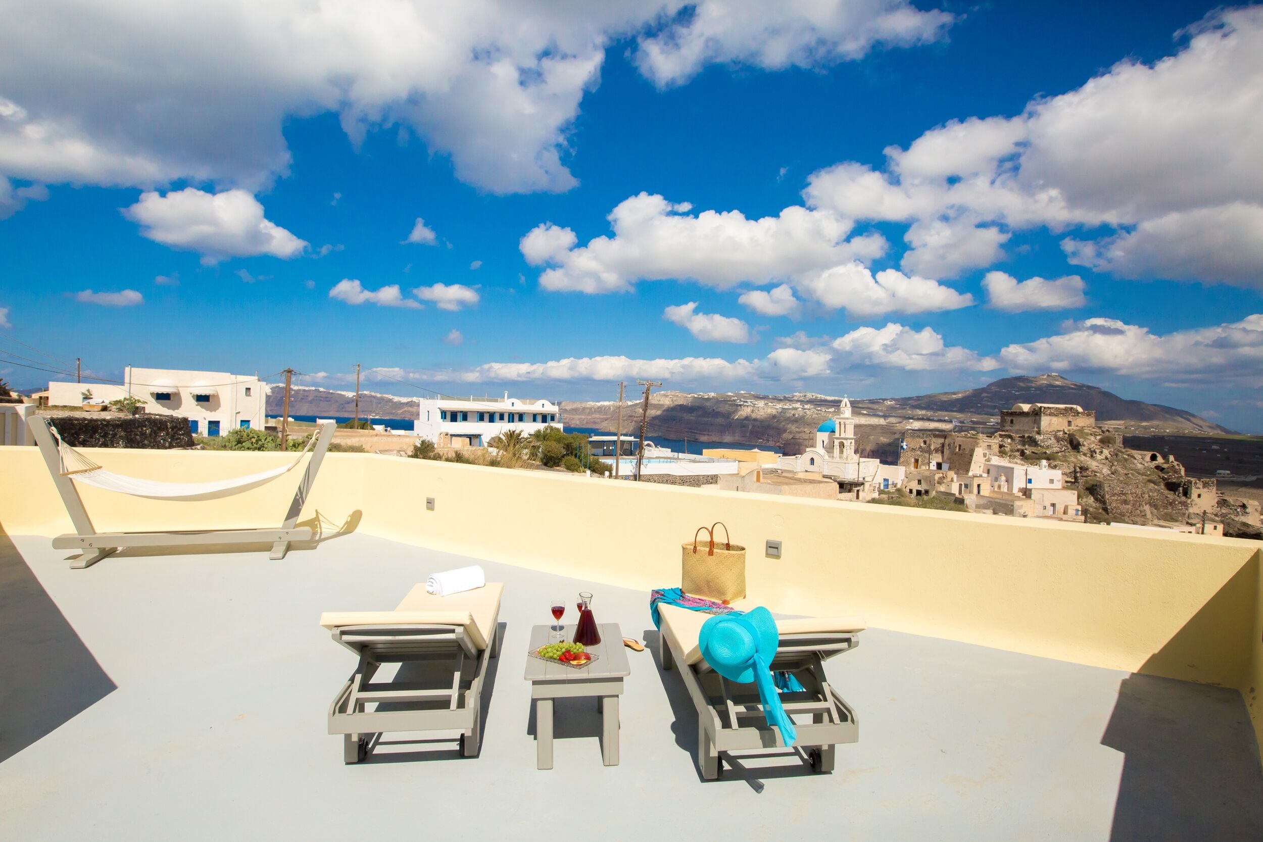 A rooftop terrace with lounge chairs, a table with a drink and snacks, and a view of the city and mountains.