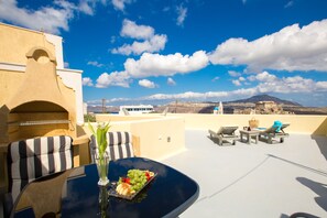A rooftop terrace with a table set for dining, outdoor seating, and a view of a mountain. - Love Nest villa (Santorini)