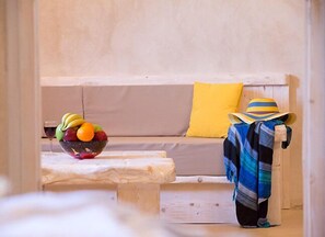 A room with a wooden bench, a bowl of fruit, and a yellow pillow on a sofa.