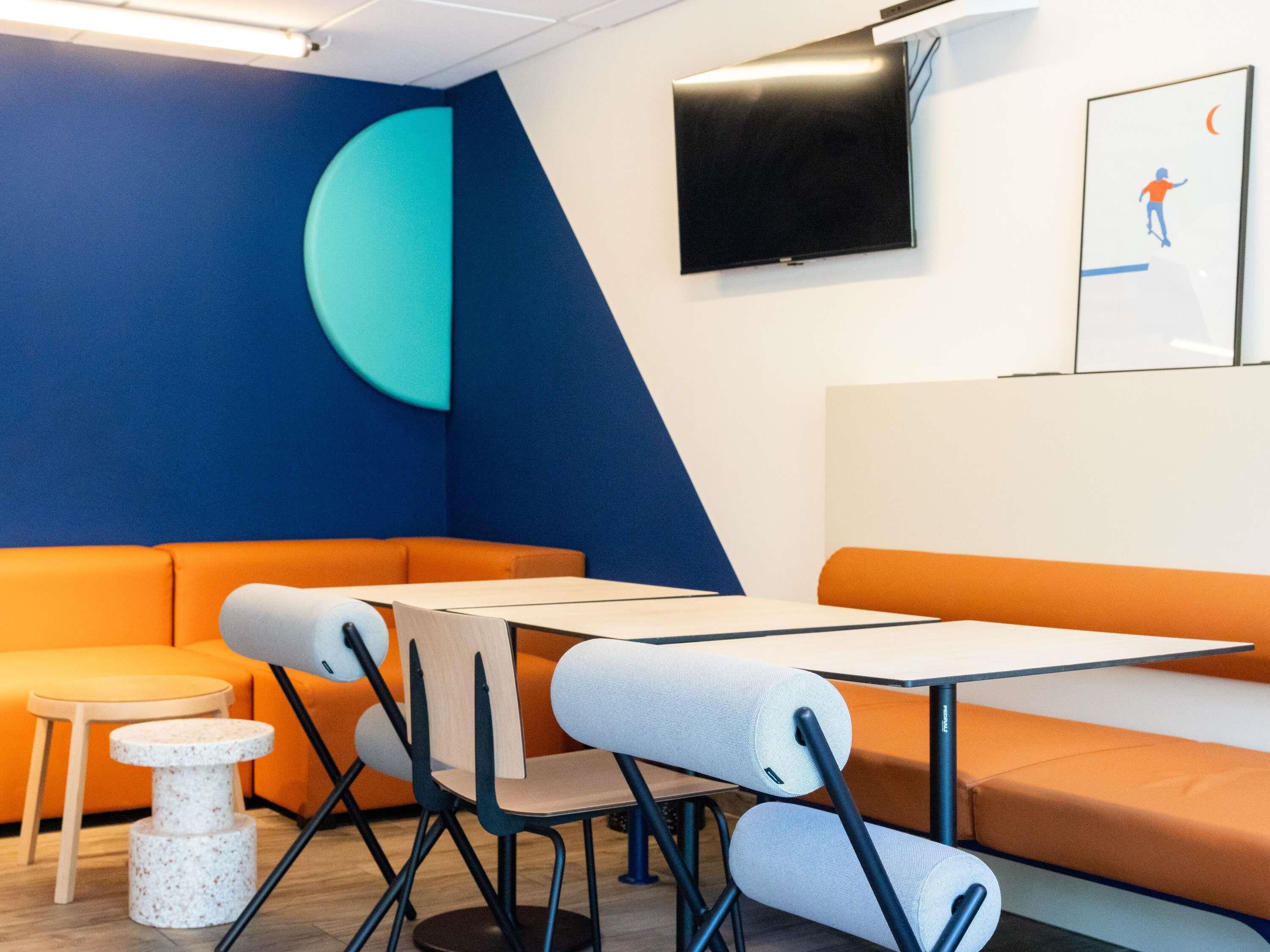 Een moderne lounge met oranje en blauwe zitplaatsen, een flatscreen-tv en een kleine tafel.