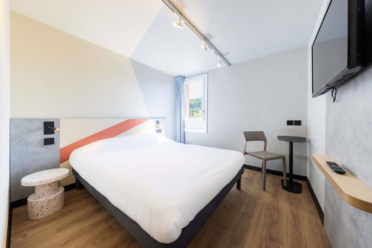 Une chambre d’hôtel moderne équipée d’un grand lit, d’un bureau, d’une chaise, d’une télévision et d’une petite table.