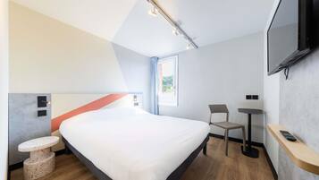 Une chambre d’hôtel moderne équipée d’un grand lit, d’un bureau, d’une chaise, d’une télévision et d’une petite table.