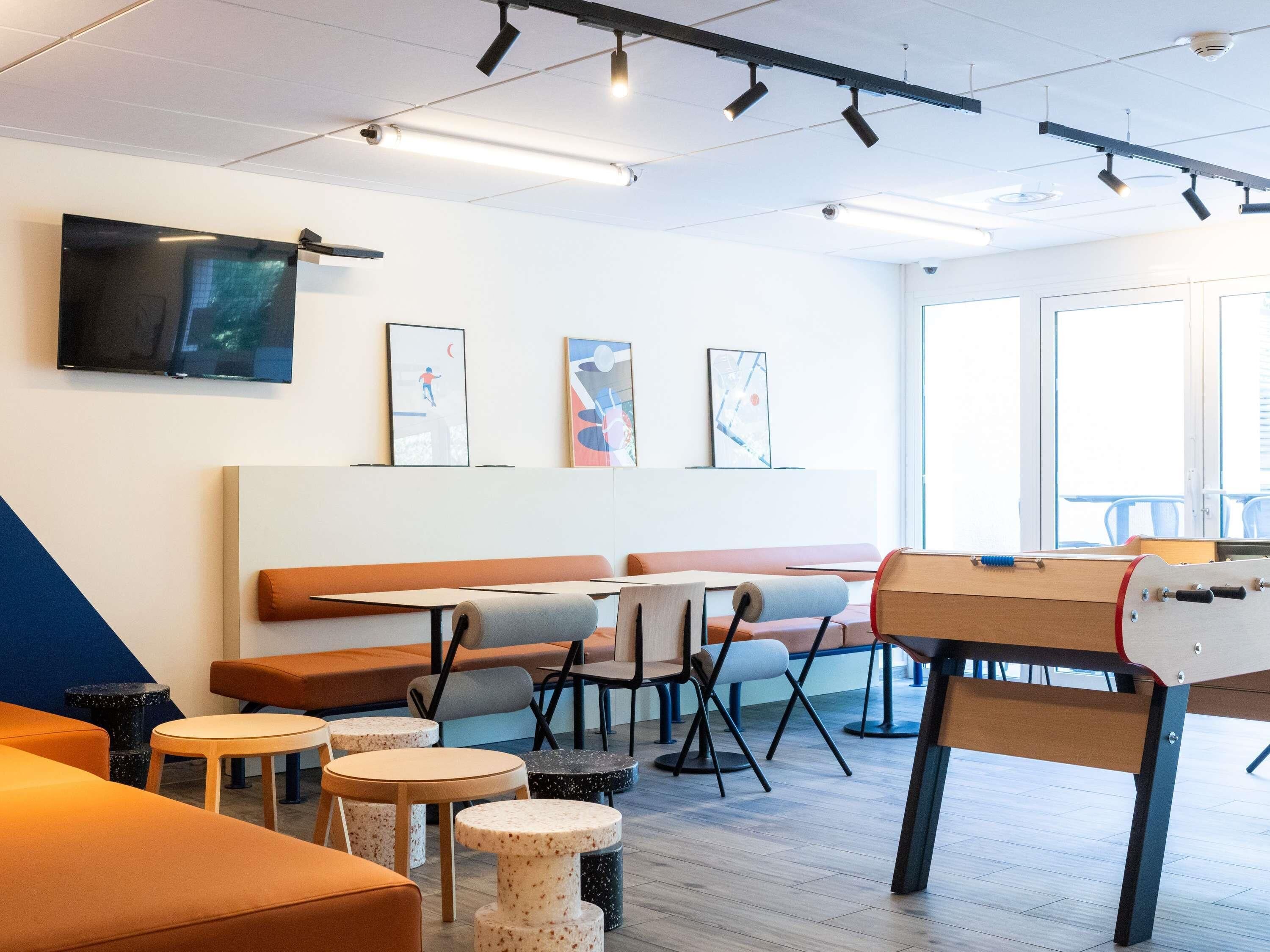 A modern interior with a long bench, round tables, and a ping pong table.