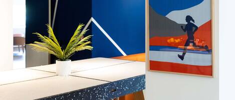 Un espacio de oficina moderno con una decoración en tonos azul y blanco, una planta en maceta sobre una mesa y una obra de arte enmarcada en la pared.