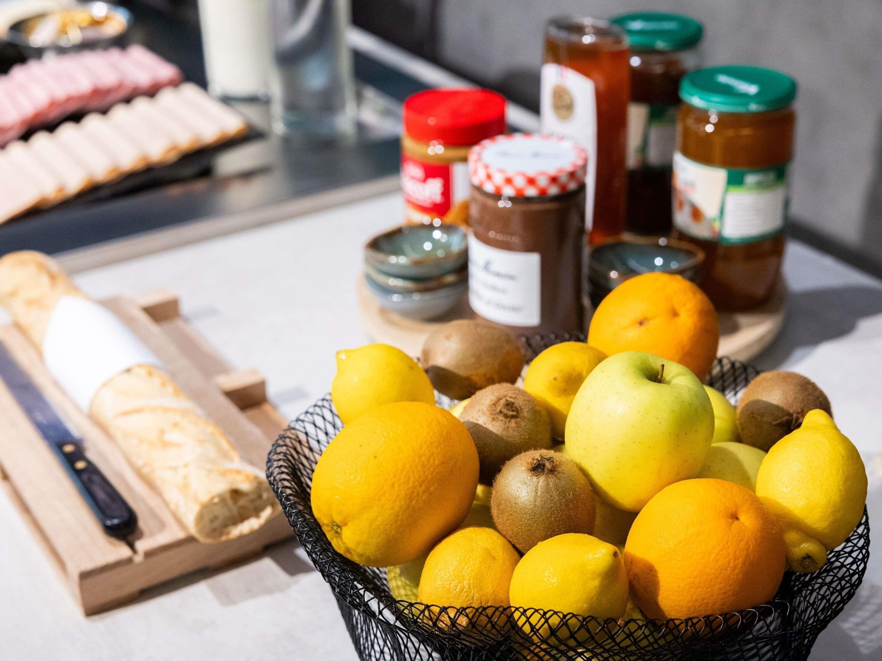 A kitchen counter with a basket of fruits, a loaf of bread, and jars of condiments.