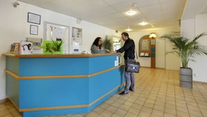 Ein Empfangstresen mit blauer Arbeitsfläche, eine Rezeptionistin und ein Gast im Gespräch.