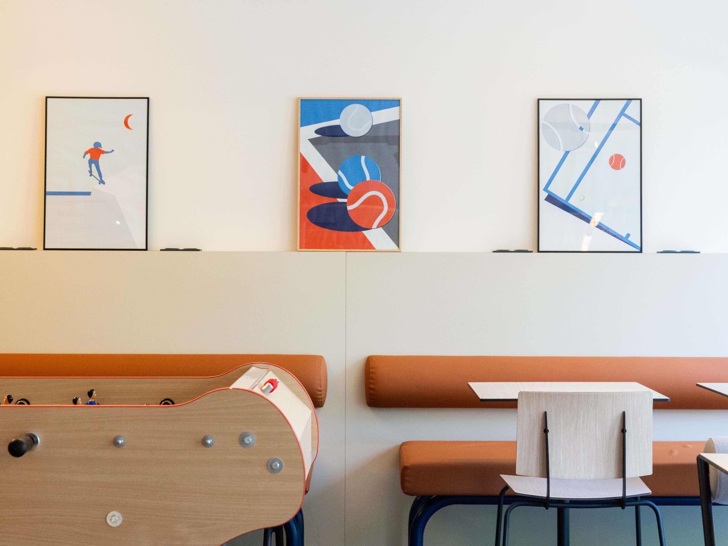 Une pièce avec une table en bois, des sièges orange et une œuvre d’art abstraite au mur.