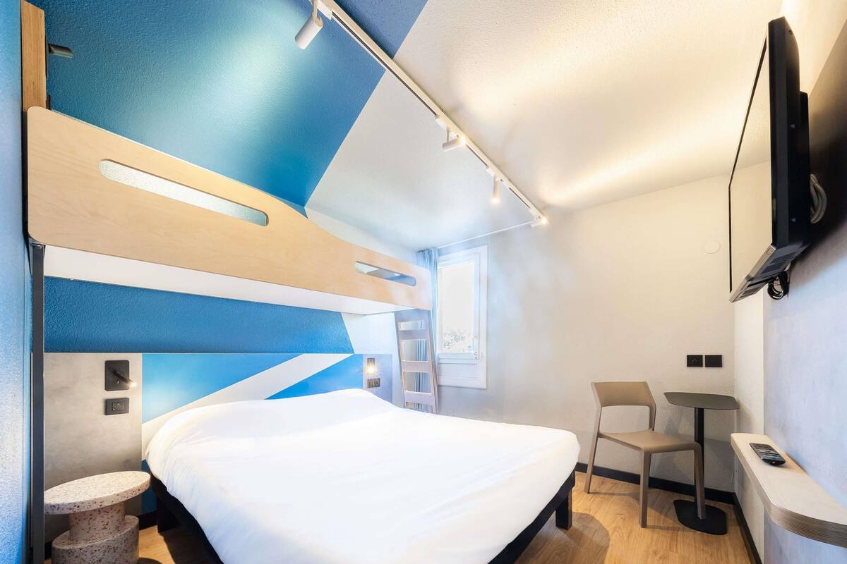 Une chambre d’hôtel moderne, dotée d’un grand lit, d’un bureau, d’une chaise et d’un téléviseur fixé au mur.