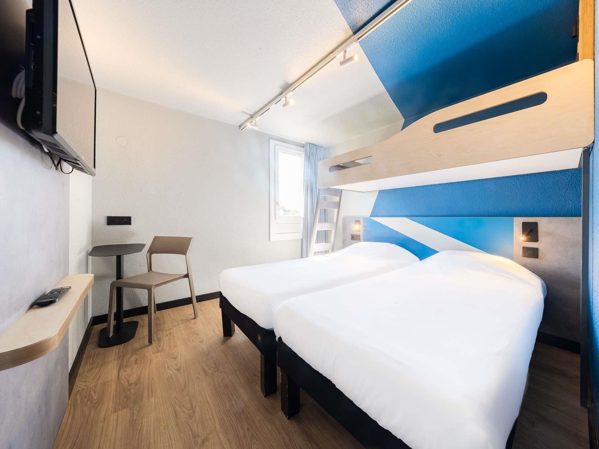 A modern hotel room with a bed, a desk, a chair, and a TV.