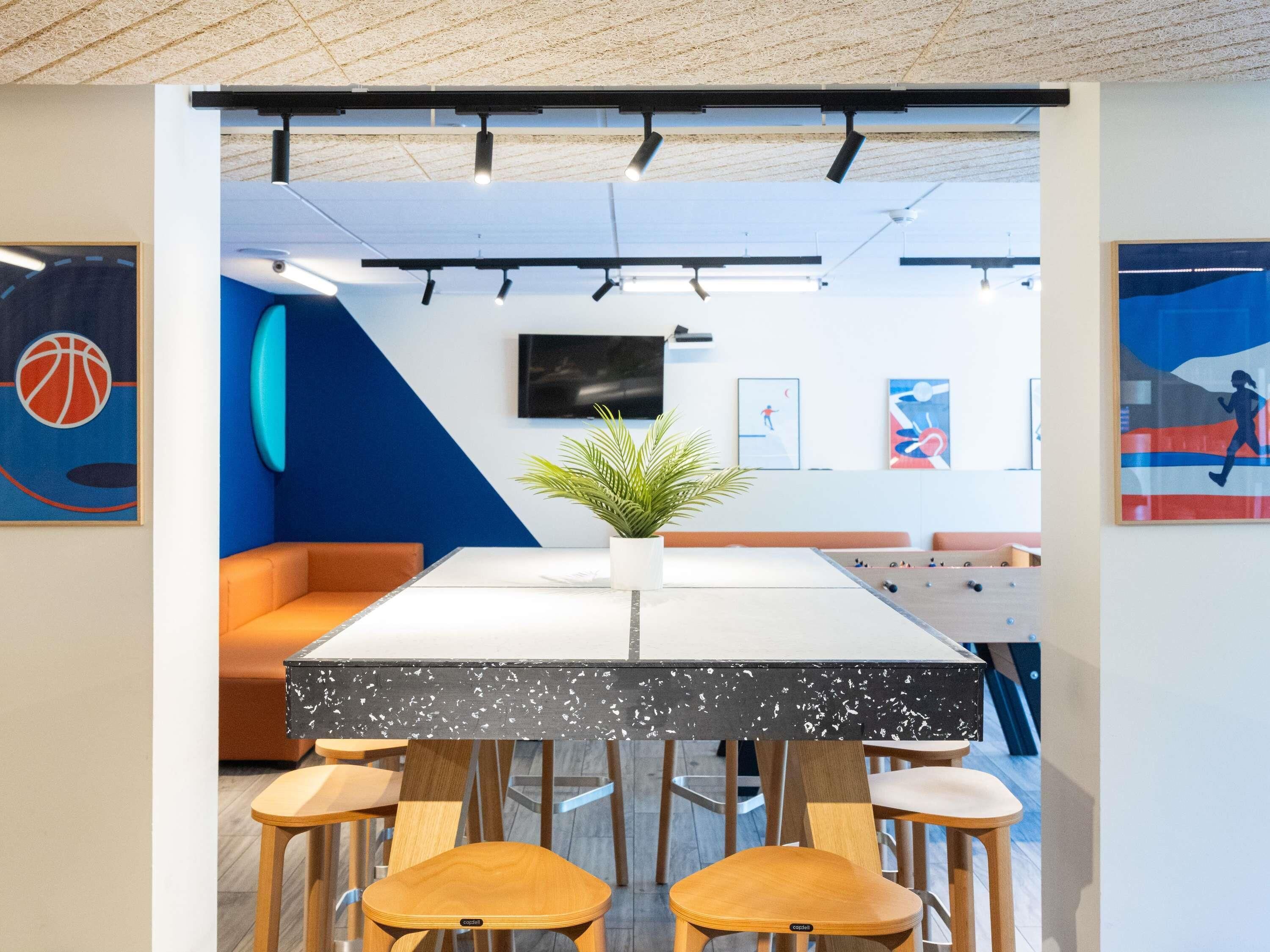 Ein modernes Interieur mit einem langen Tisch, Stühlen, einem Kicker und Sportmotiven.