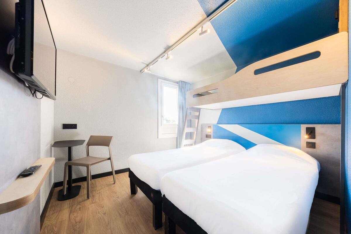 Une chambre d’hôtel moderne équipée d’un lit, d’un bureau, d’une chaise et d’un téléviseur fixé au mur.