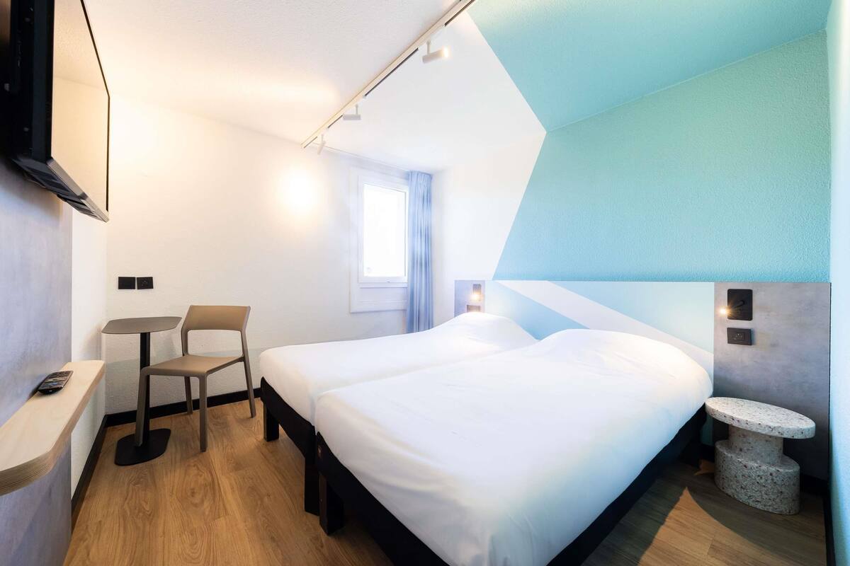 Moderni hotellihuone, jossa on sänky, työpöytä, tuoli ja televisio.