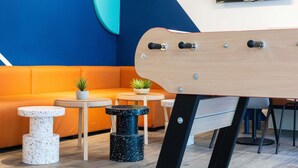 Ein moderner Lounge-Bereich mit blau-orange Farbschema, ausgestattet mit einer Couch, kleinen Tischen und einer Gitarre.