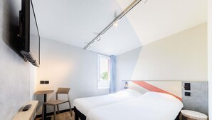 Ein Hotelzimmer mit einem Bett, einem Schreibtisch, einem Sessel, einem Fernseher und einem Fenster.