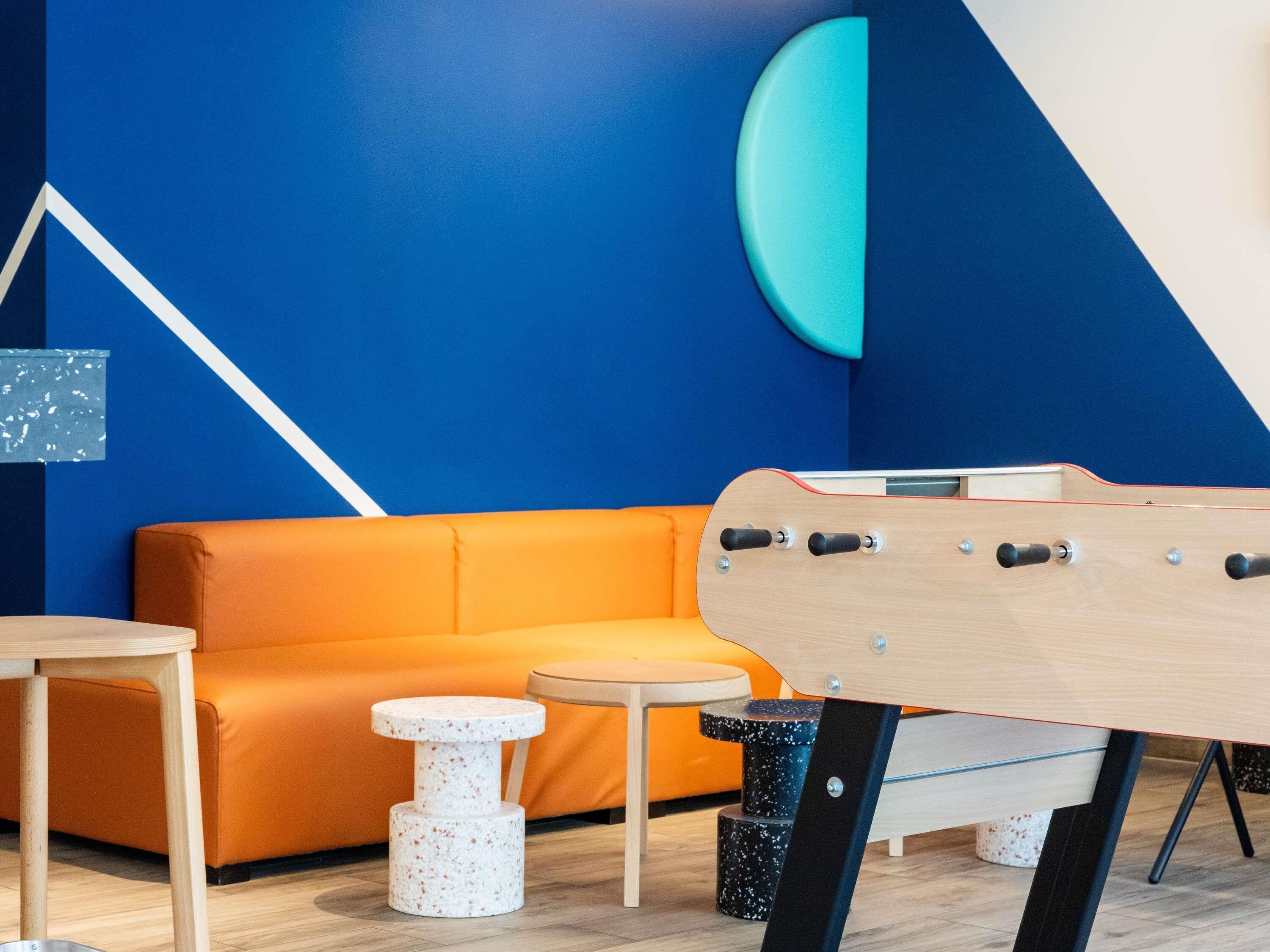 Un interior moderno con una pared azul, una guitarra de madera, una mesa de madera, un rascador para gatos blanco y un sofá naranja.