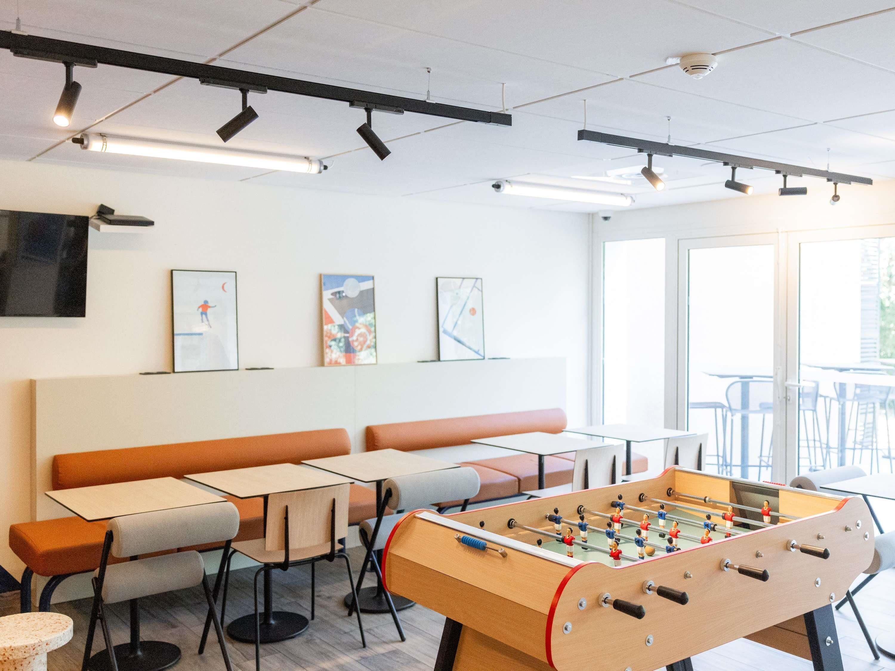 A modern indoor space with tables, benches, and a foosball table.