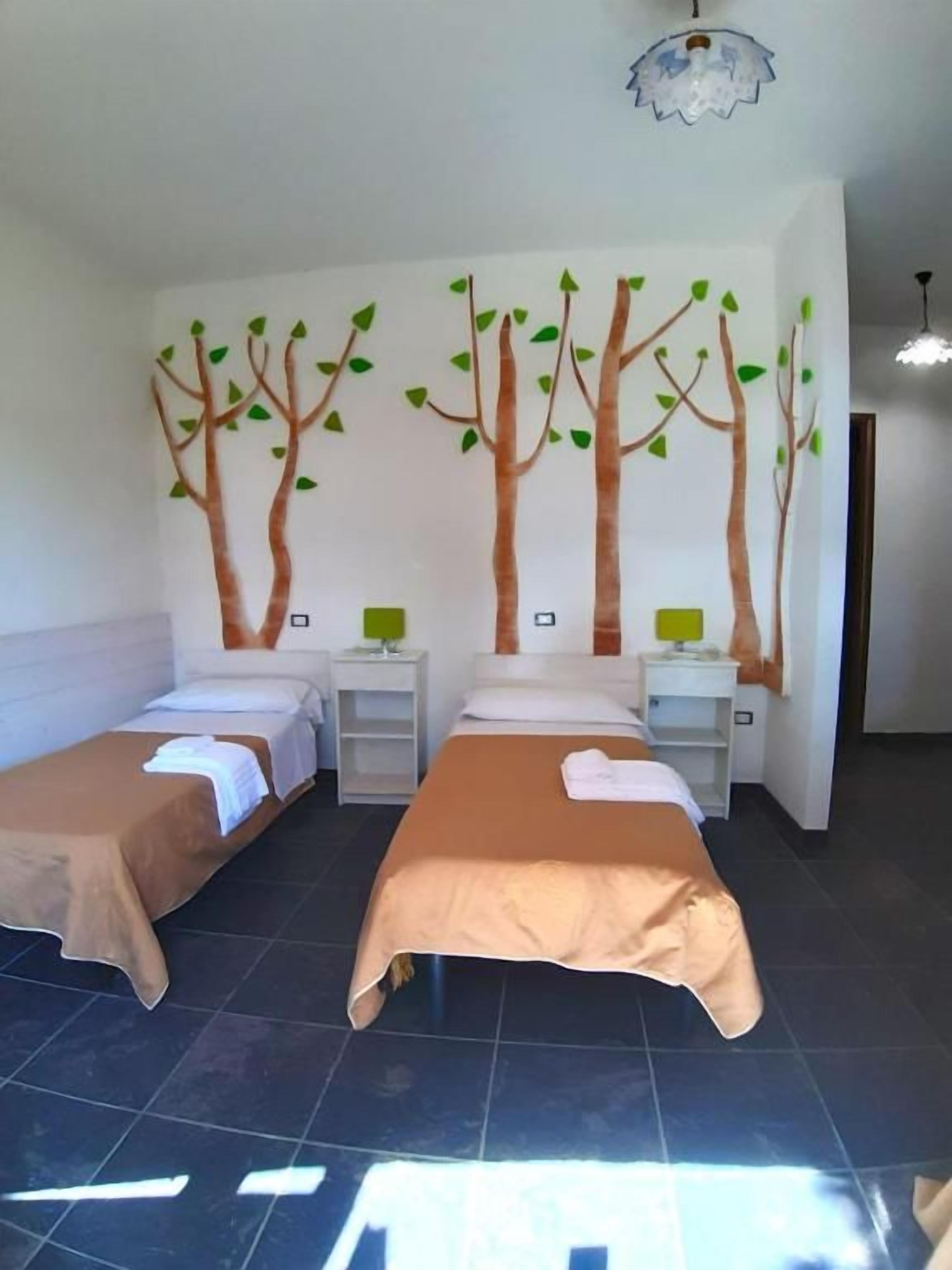 Ein Zimmer mit zwei Betten, einer Baum-Wandmalerei und einem Fliesenboden.