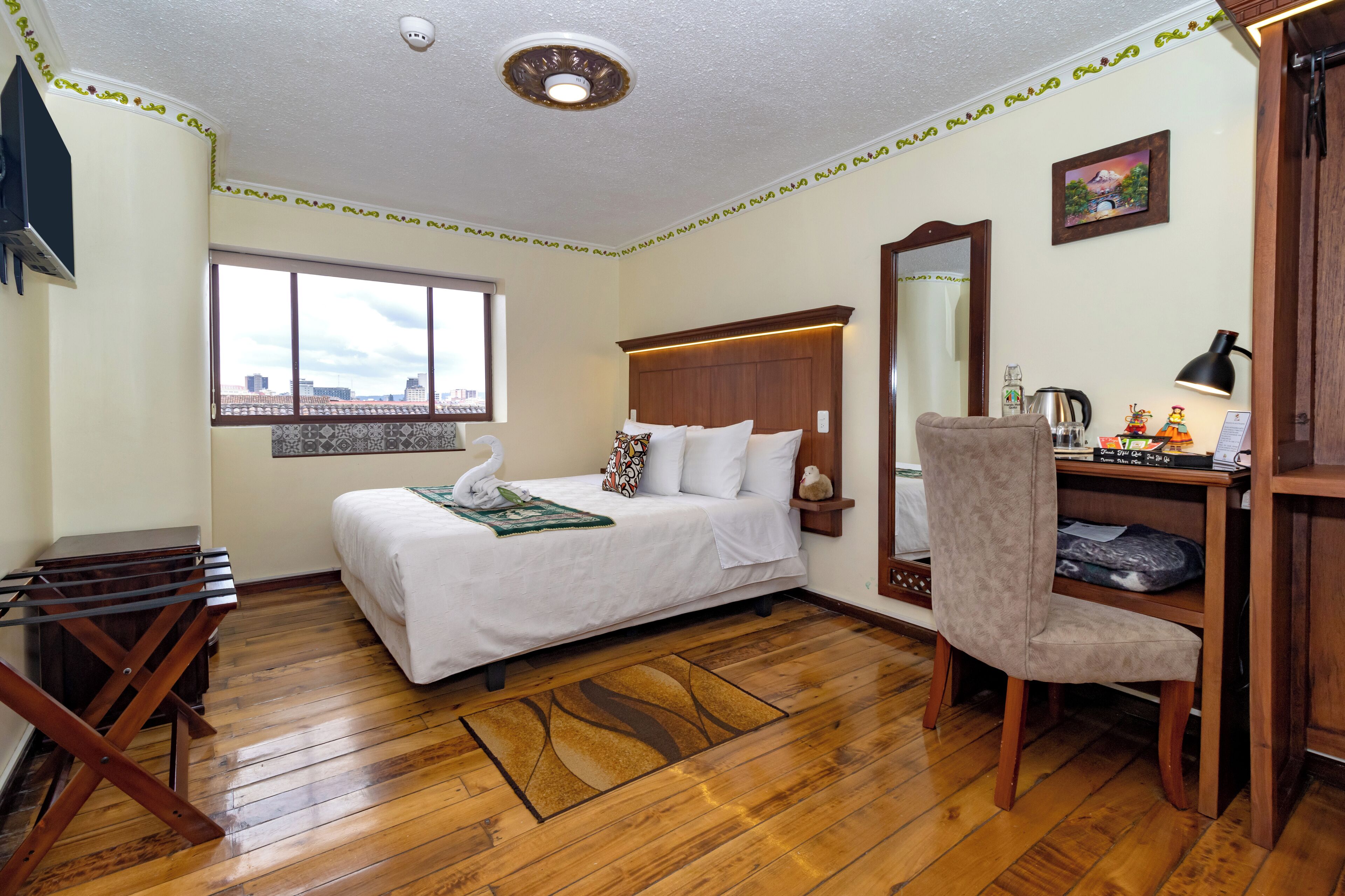 A hotel room with a bed, a chair, a desk, a window, and a mirror.