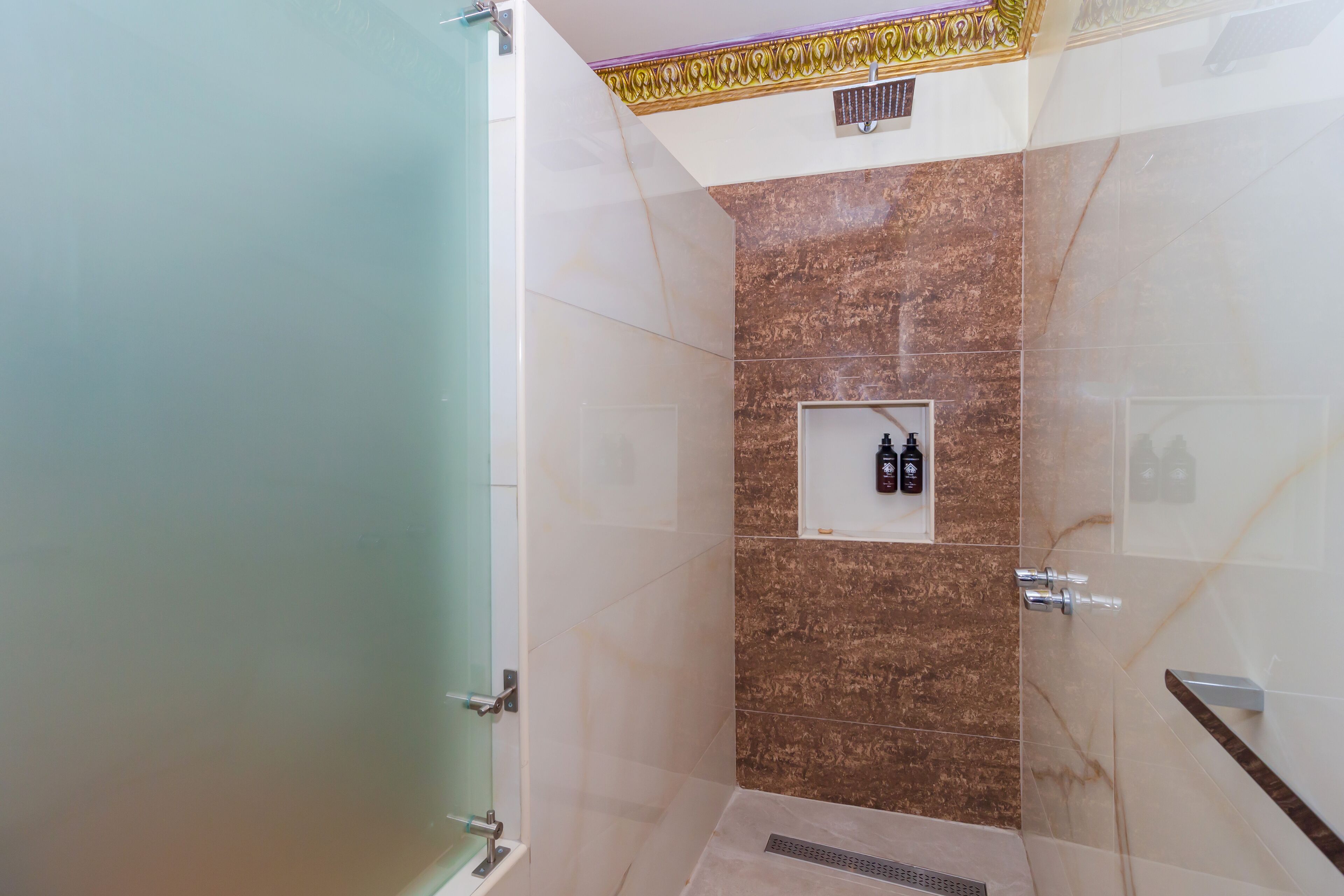 A modern bathroom with marble walls, a glass shower enclosure, and a built-in shelf with toiletries.
