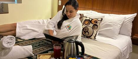 A hotel room with a bed, a tray with breakfast items, a kettle, and a pillow with a patterned design.