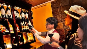 Una zona de bar con un botellero, una cafetera y una persona sirviendo vino.