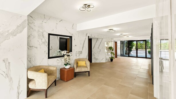 A spacious lobby with marble walls, two armchairs with yellow cushions, a small wooden side table, and a large mirror. - Sonesta Essential Atlantic City West (Egg Harbor Township)