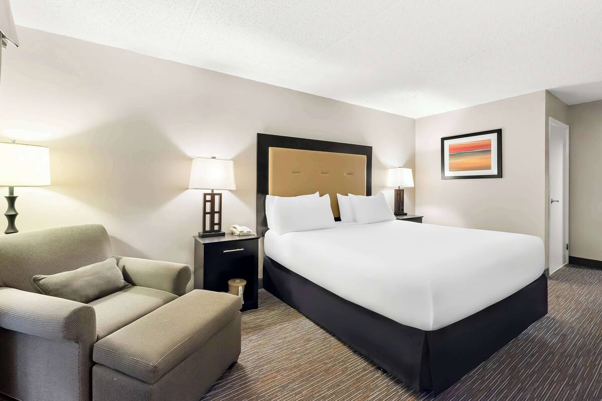 A hotel room with a large bed, a sofa, a nightstand with a lamp, and a framed picture on the wall.