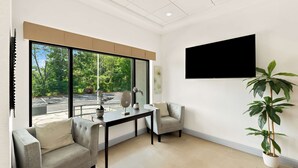 A modern living room with a sofa, armchair, and a table with a fan. A large window offers a view of trees and a parking lot. - Sonesta Essential Atlantic City West (Egg Harbor Township)