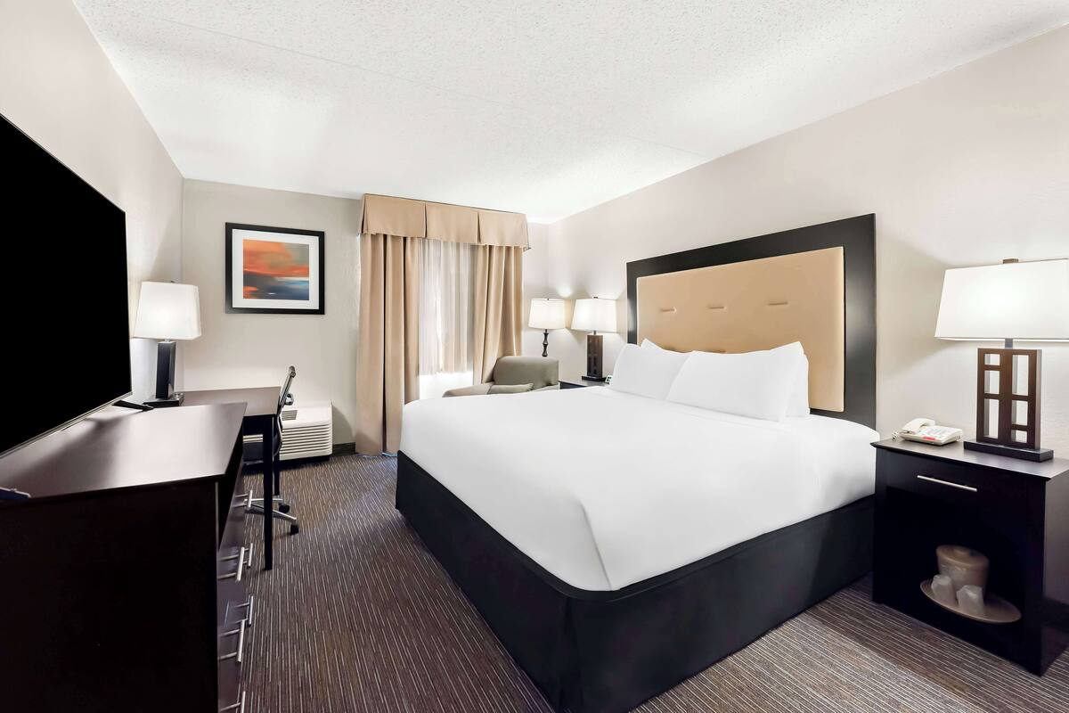 A hotel room with a large bed, two bedside tables with lamps, a desk with a chair, and a television.