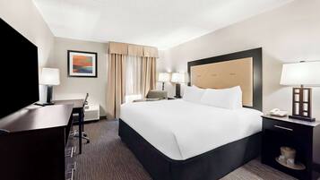 A hotel room with a large bed, two bedside tables with lamps, a desk with a chair, and a television.