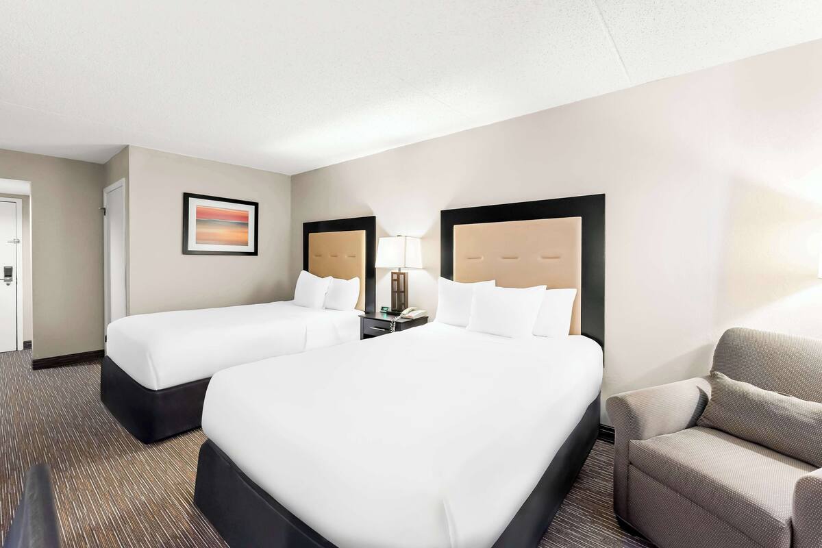 A hotel room with two beds, a desk, a chair, and a framed picture on the wall.