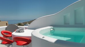 A modern outdoor pool area with a curved edge, red chairs, and a view of the sea. - Drops villas (Santorini)