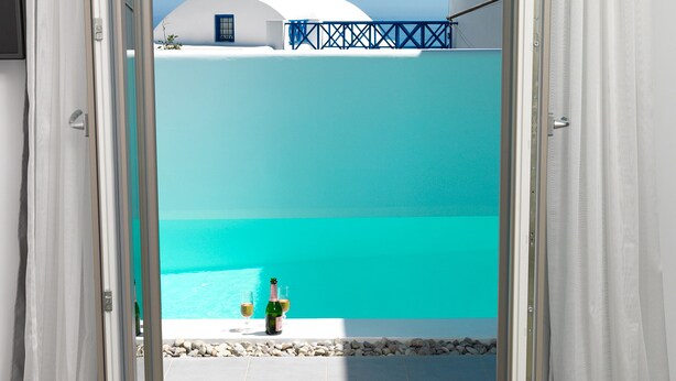 A doorway leading to a balcony with a view of a turquoise sea and white buildings. - Drops villas (Santorini)